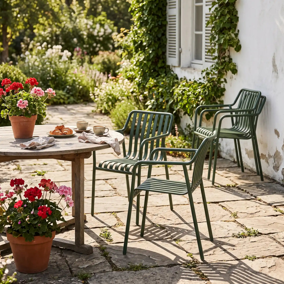 Dark green stackable aluminium chairs with armrests at a garden table, with two chairs stacked by the wall